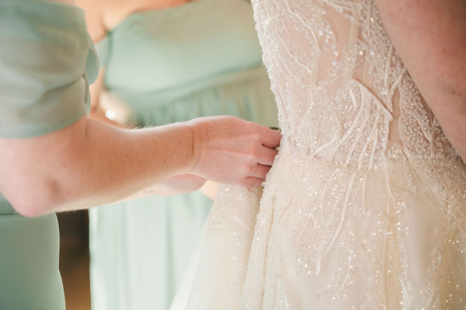 Bridesmaid carefully fastening the back of a beaded ivory wedding gown before the ceremony.