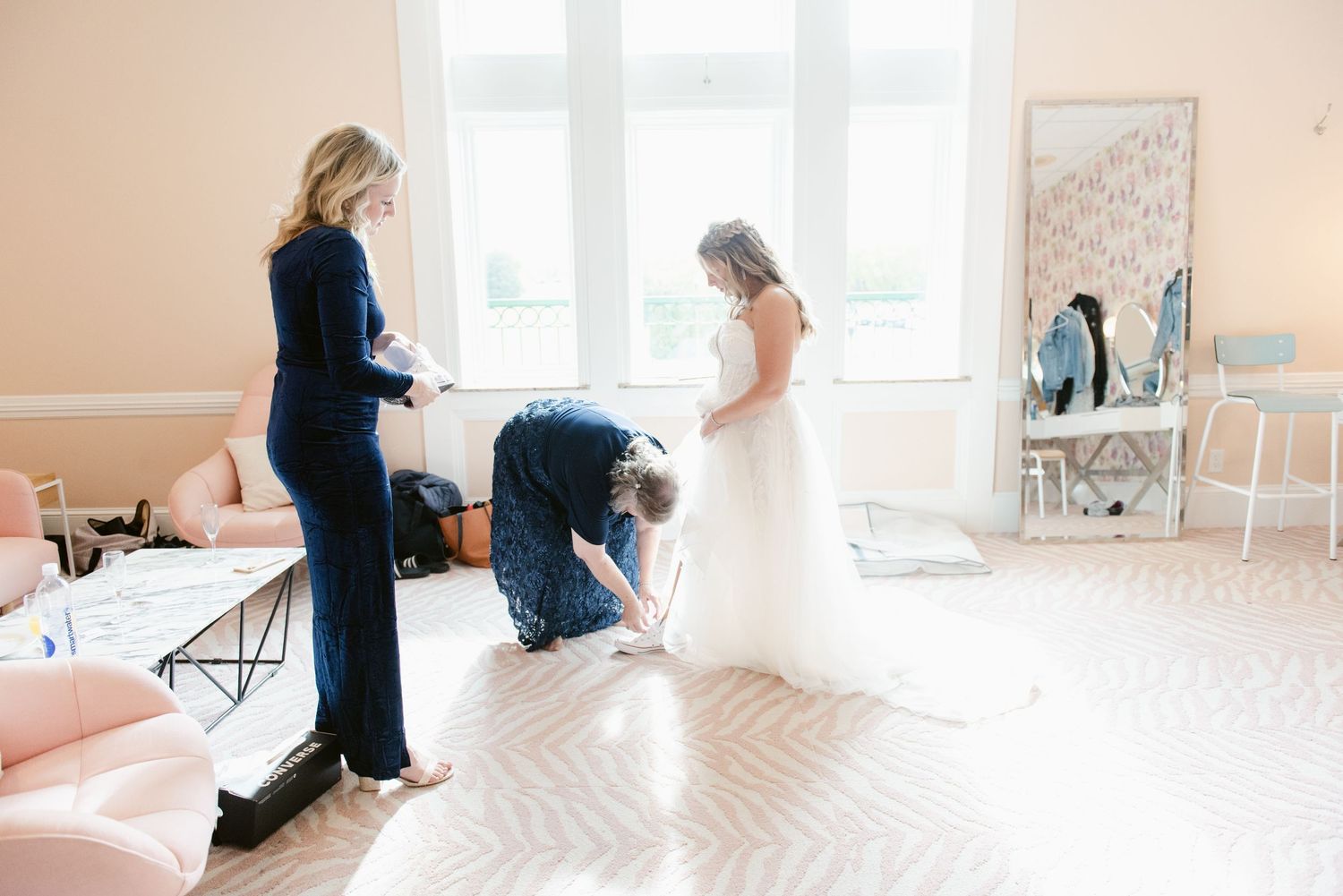 Central MN Wedding Photos | Bride in white wedding gown being assisted by two attendants in a soft pink bridal suite before ceremony.
