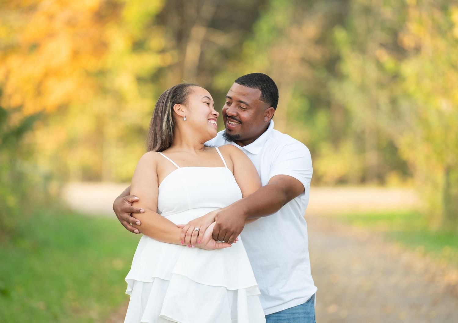 Central Minnesota Best Engagement Photo A happy couple embraces and smiles on a scenic tree-lined path with autumn foliage in the background