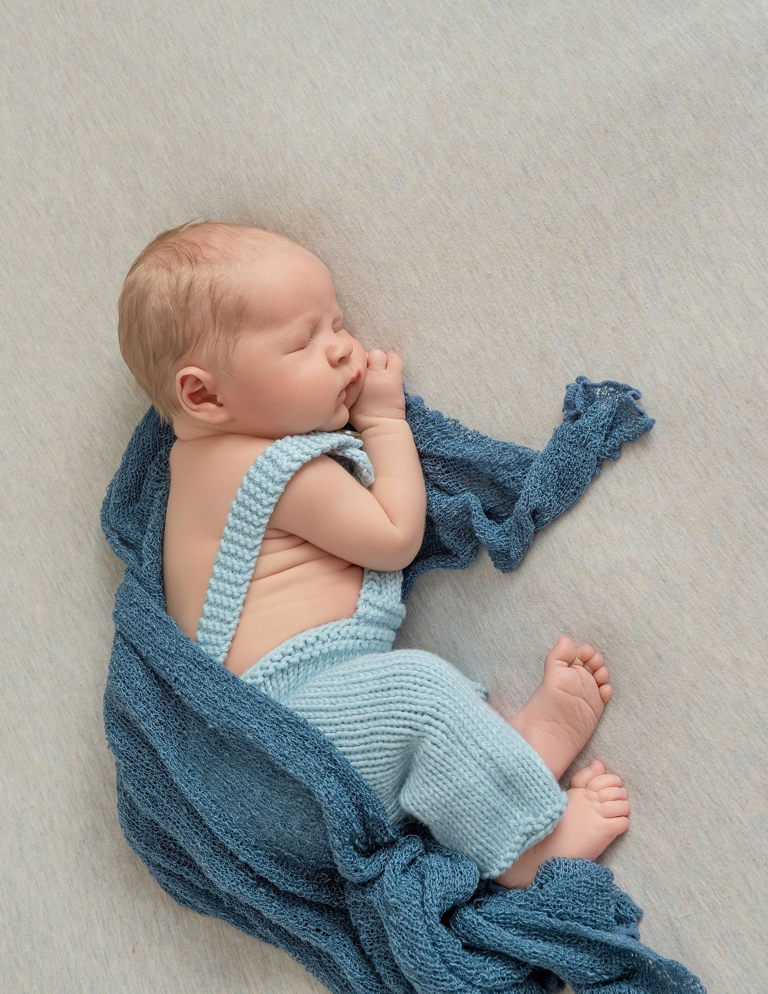 In central Minnesota a Peaceful newborn baby wrapped in blue textiles sleeping on light gray background.