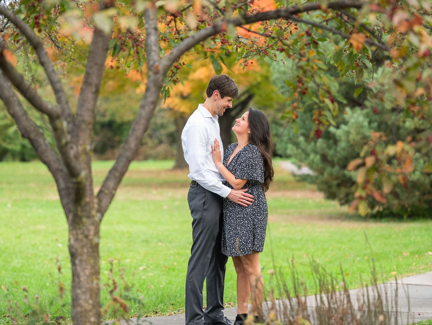 Central MN Engagement Session. a romantic couple embraces under autumn trees with colorful fall foliage in a peaceful park setting.