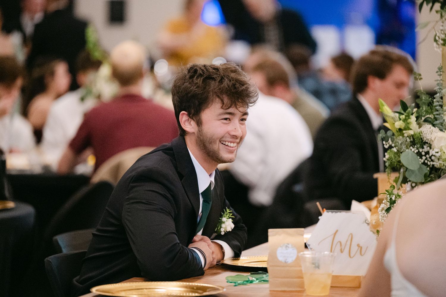 Wedding reception guests share laughs and conversations at long wooden tables.