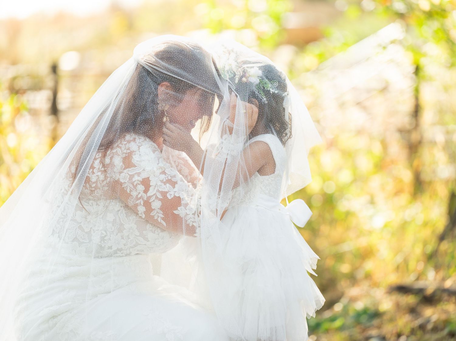 A bride in a white wedding dress and veil stands in a sun-dappled forest with golden autumn foliage.