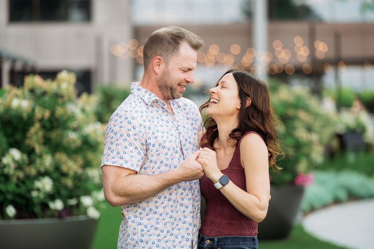A couple shares a romantic moment outdoors in a garden setting with string lights and greenery.