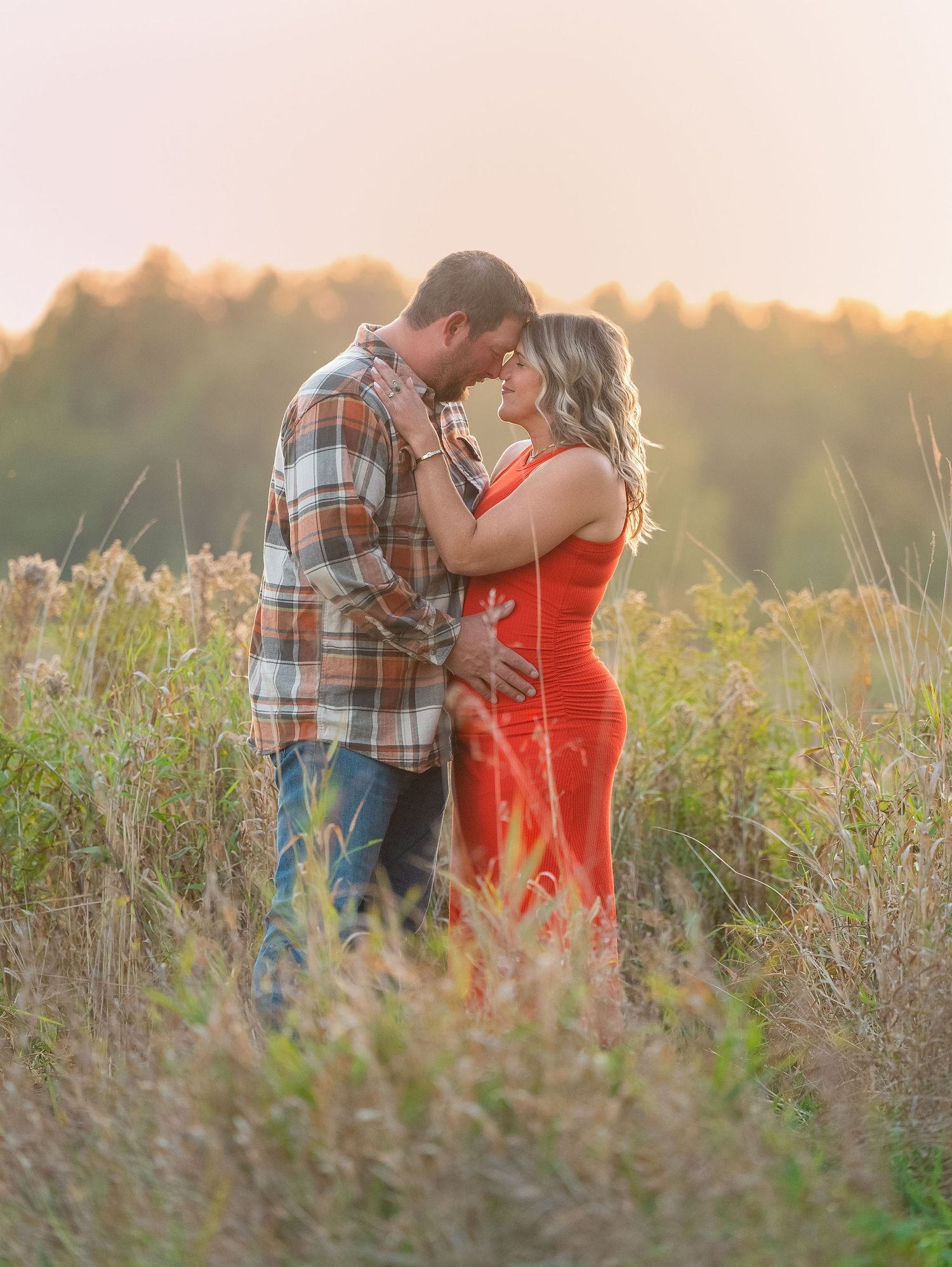 Romantic couple embracing in a golden field at sunset with soft lighting and tall grass.
