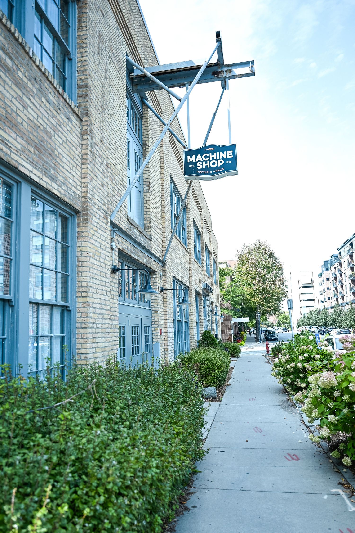 Exterior view of a brick building with blue trim and hydrangea bushes lining the sidewalk.