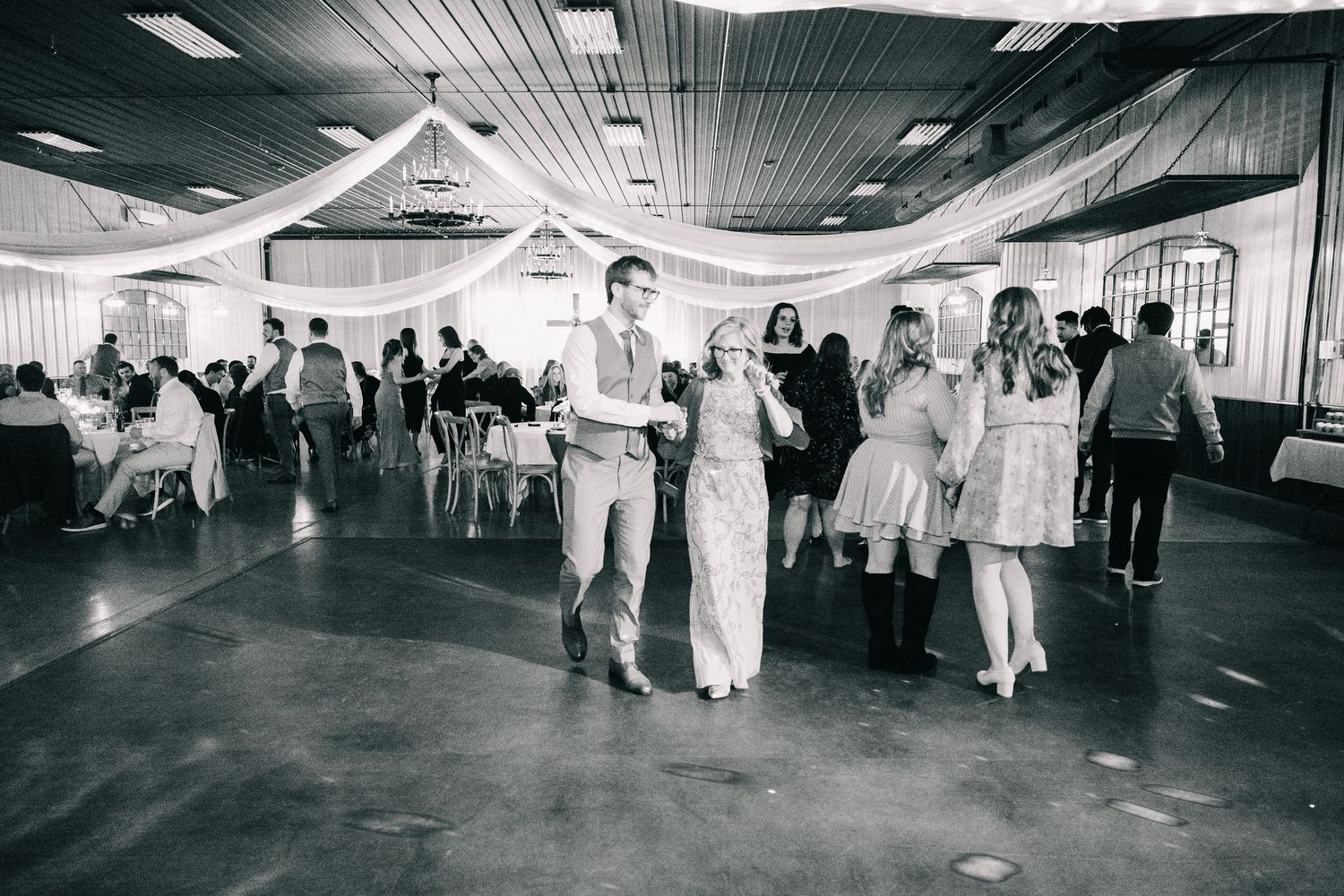 Black and white photo of couples dancing at a wedding reception in a decorated venue.