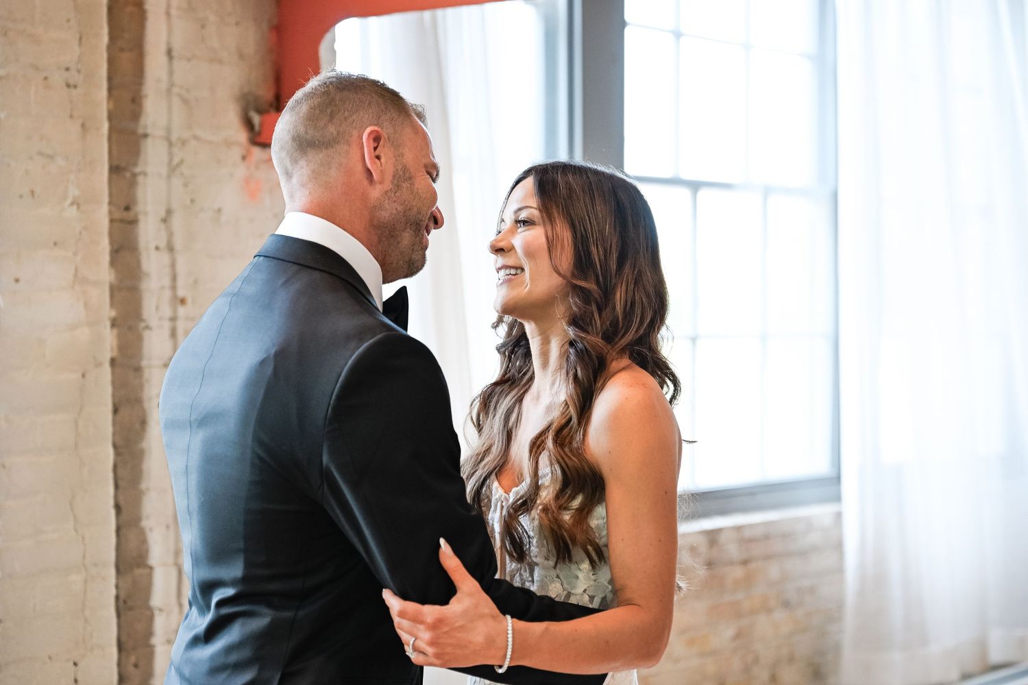 Central MN Wedding Photos | Bride and groom share a tender first look moment, smiling at each other in an elegant industrial venue.