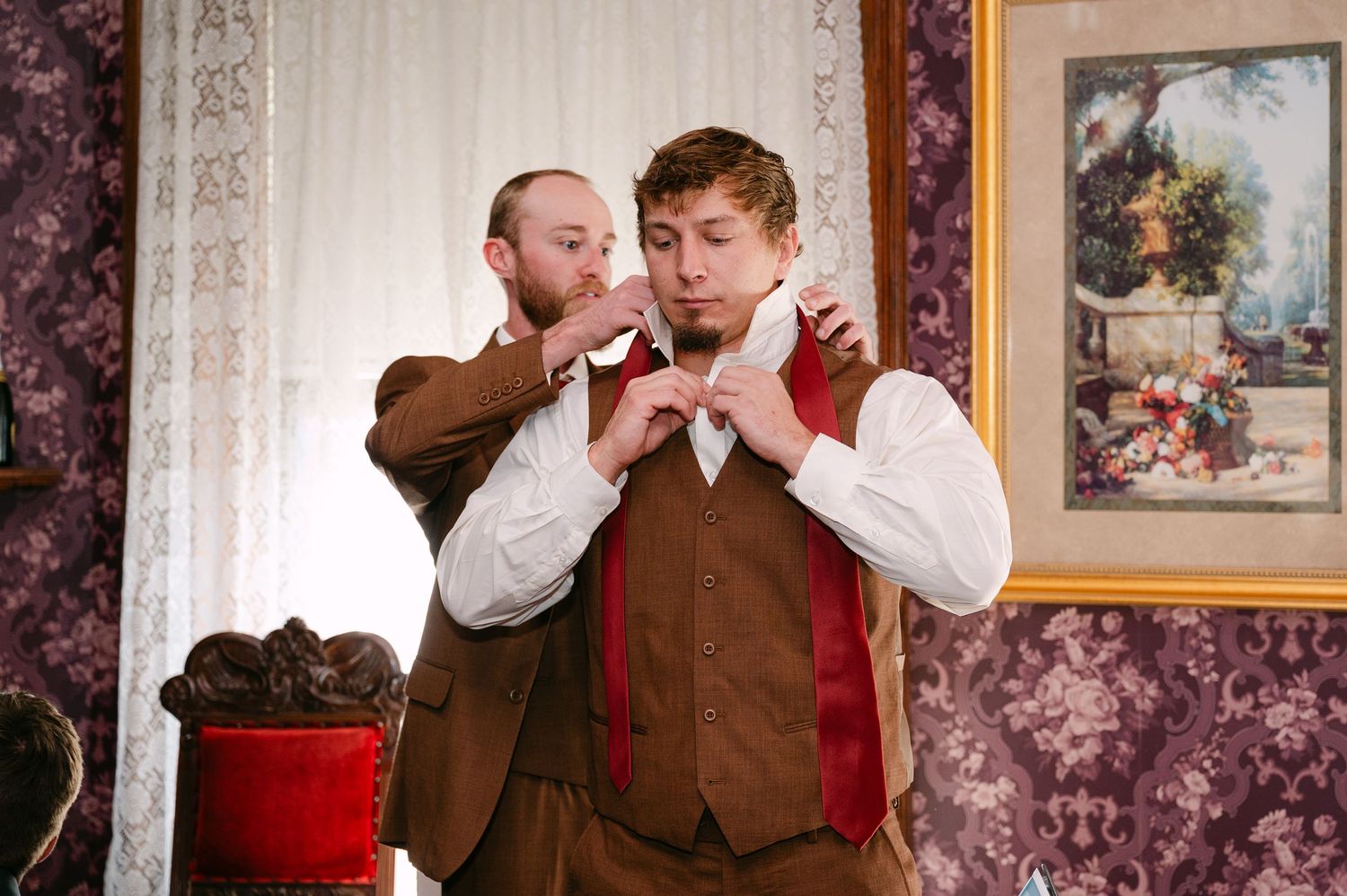 Central MN Wedding Photos | Groom getting his bow tie adjusted by groomsman while dressing for wedding ceremony in elegant room.