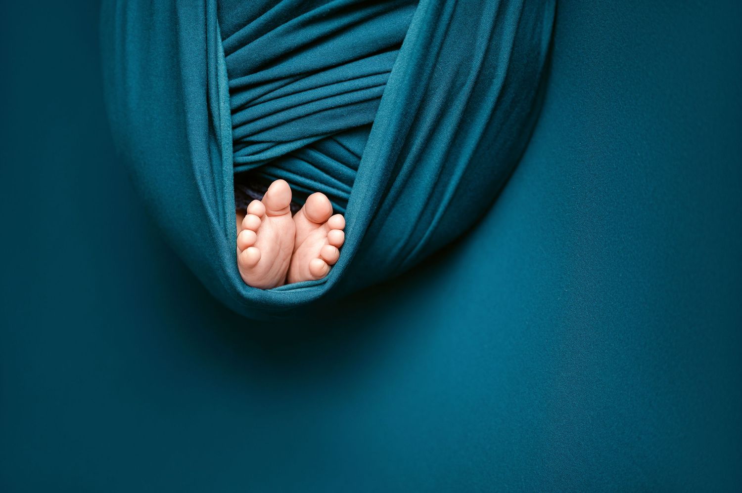 St Cloud newborn Photos of Newborn baby feet peeking out from teal fabric wrap against blue background.