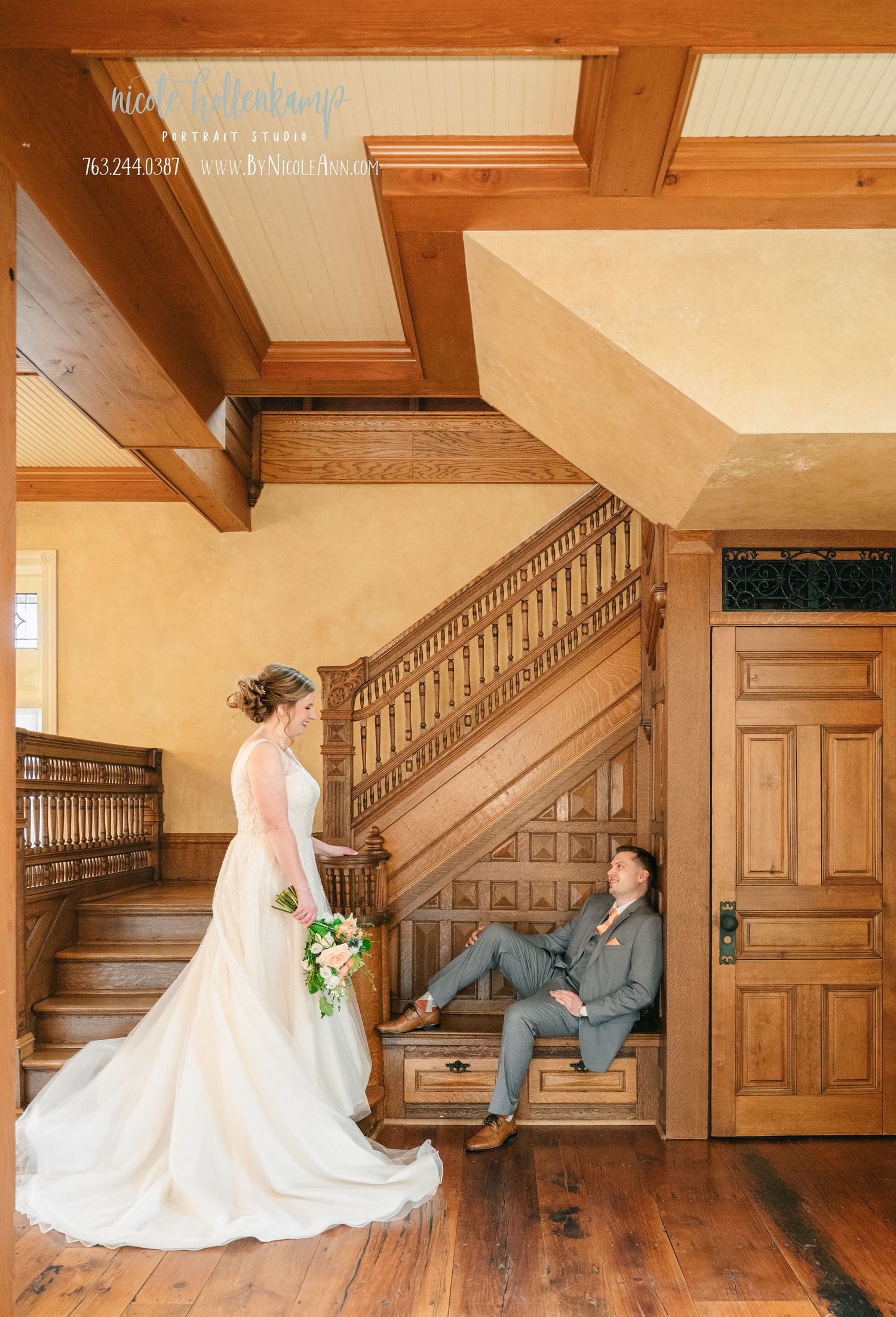Bride in white gown and groom in gray suit pose on ornate wooden staircase in elegant venue. Crooked Willow Osakis