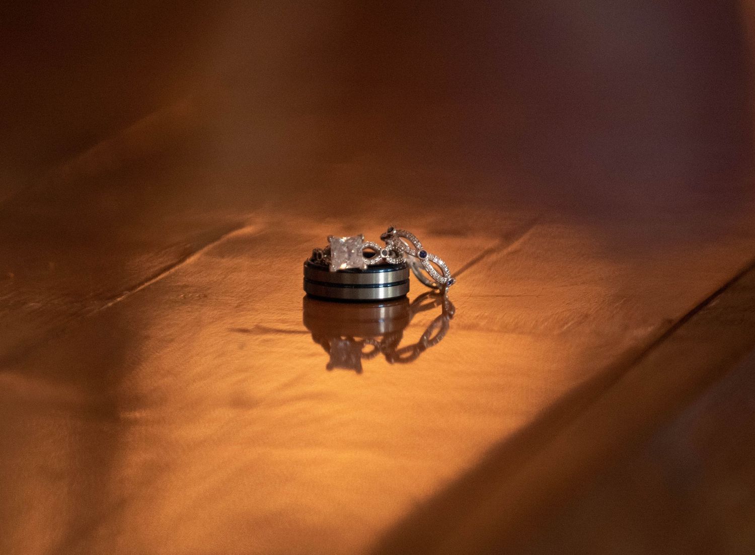 Wedding rings sit dramatically illuminated on a textured surface casting a warm glow and shadow. Zimmerman MN Weddings