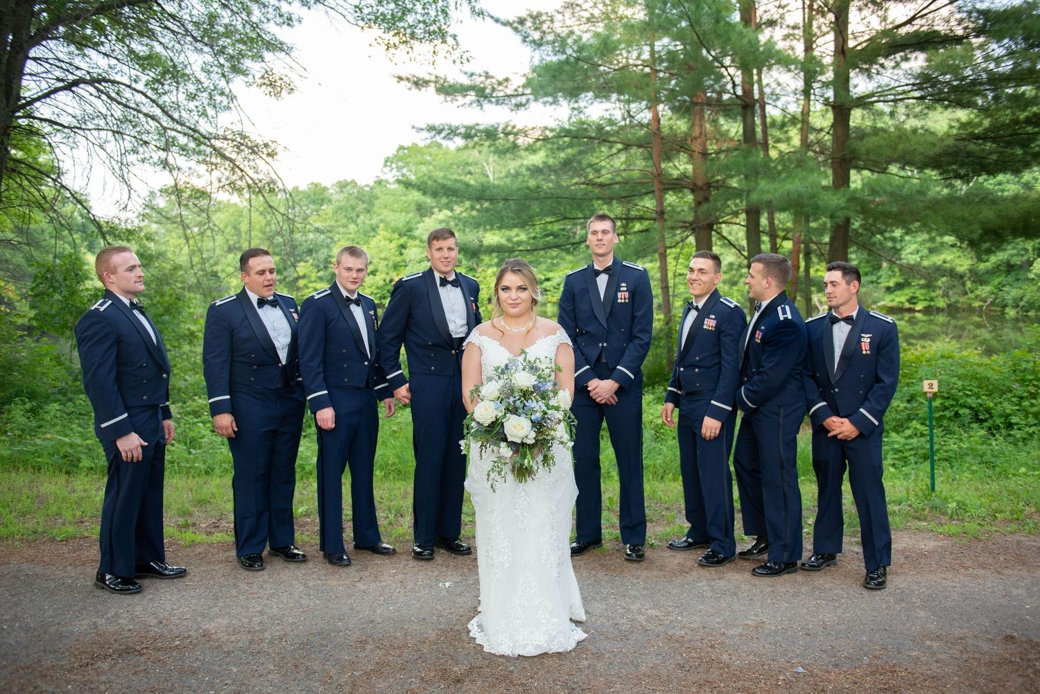 Wedding party in navy suits gathered outdoors with pine trees in the background. Zimmerman MN Weddings