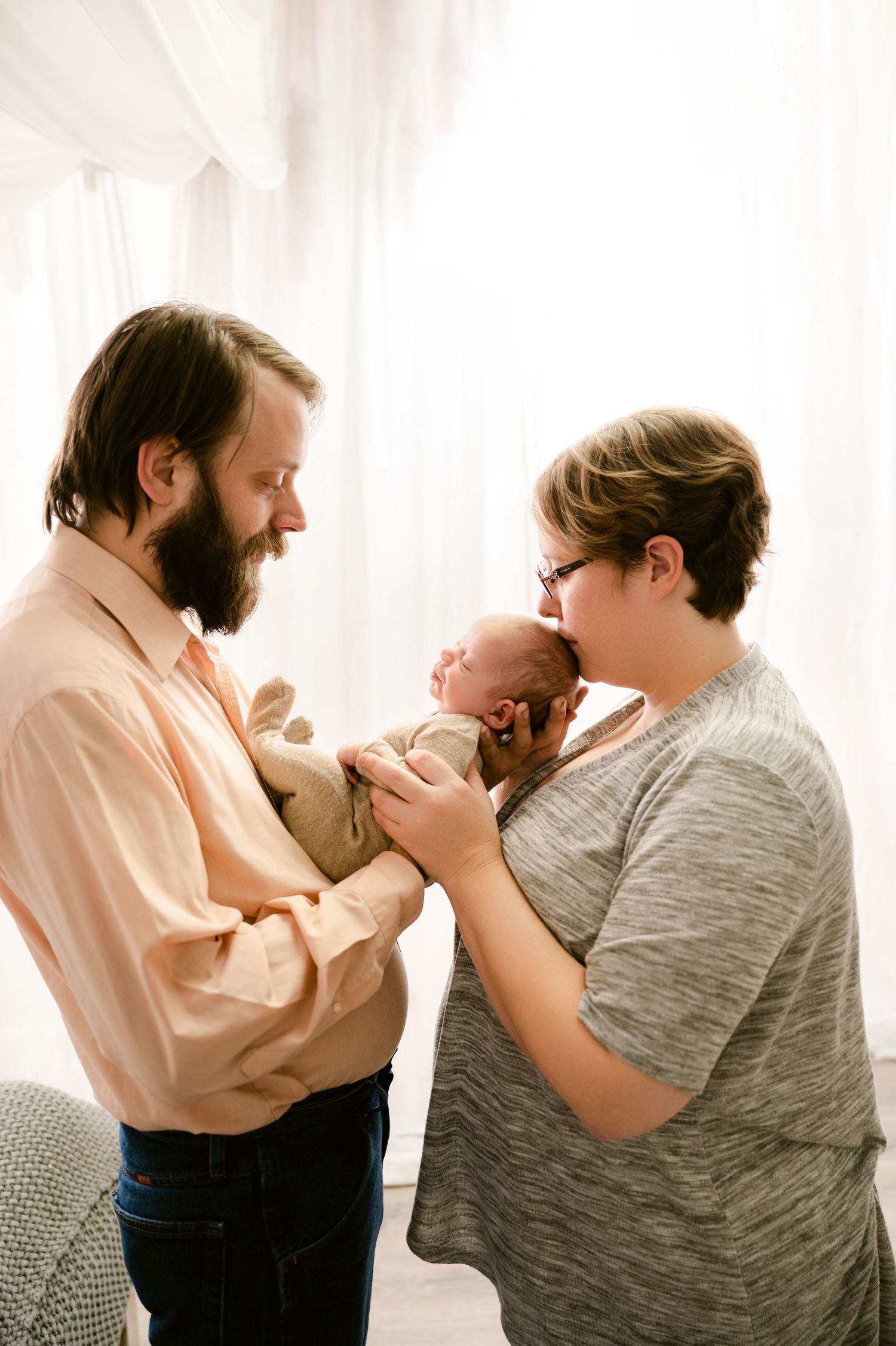 Parents share a tender moment with their newborn baby in a bright, sunlit room.