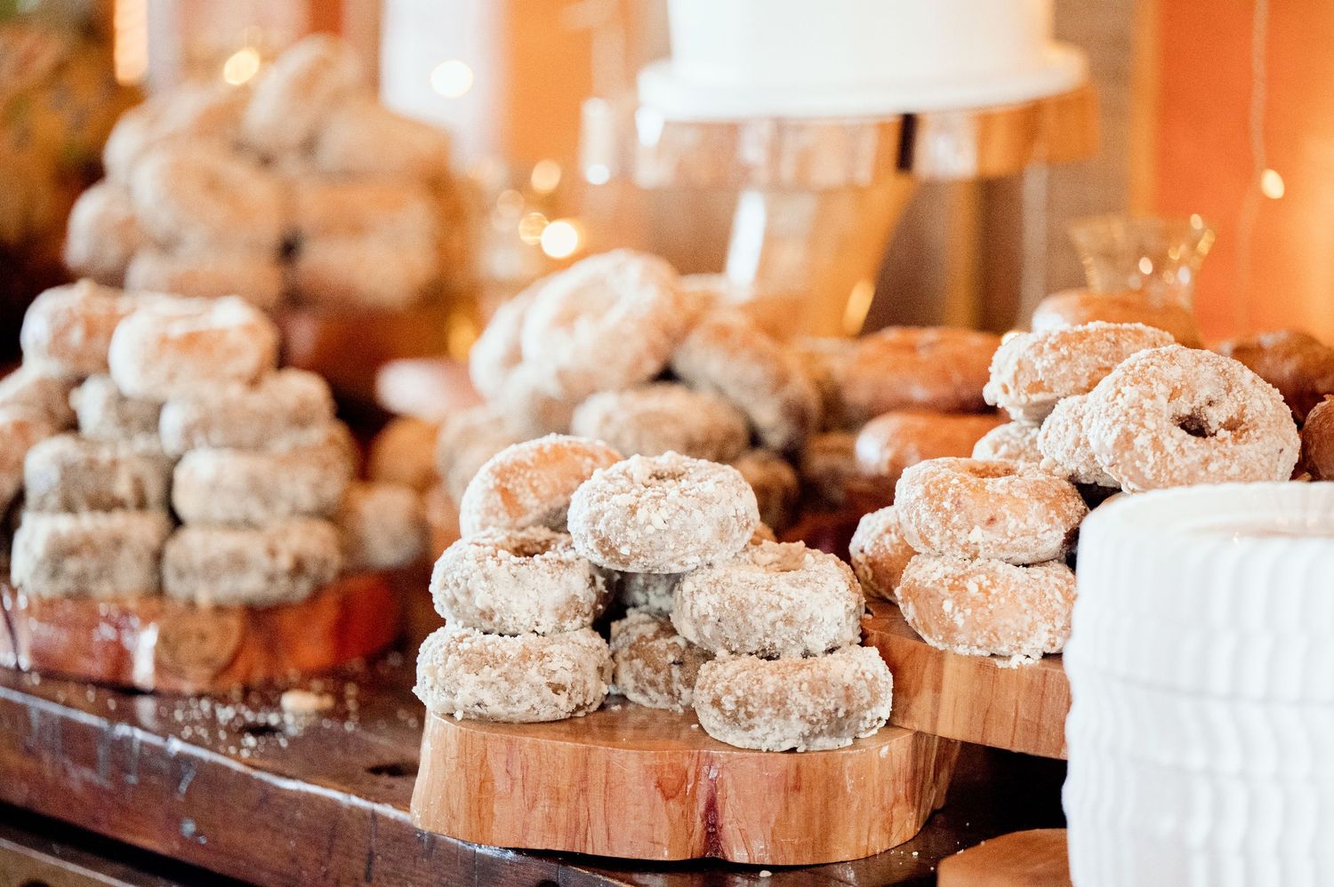 Rustic wood rounds display homemade powdered sugar donuts at a wedding dessert table.