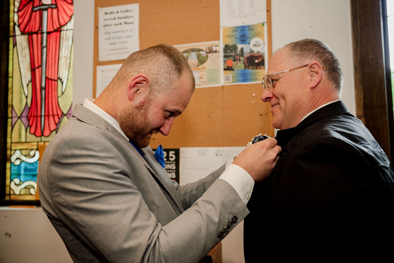 Two clergy members sharing a collegial moment in front of a church bulletin board.