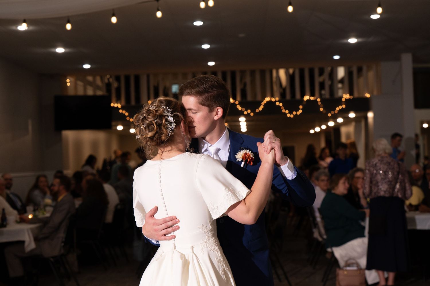 A couple shares their first dance under romantic string lights at their wedding reception.