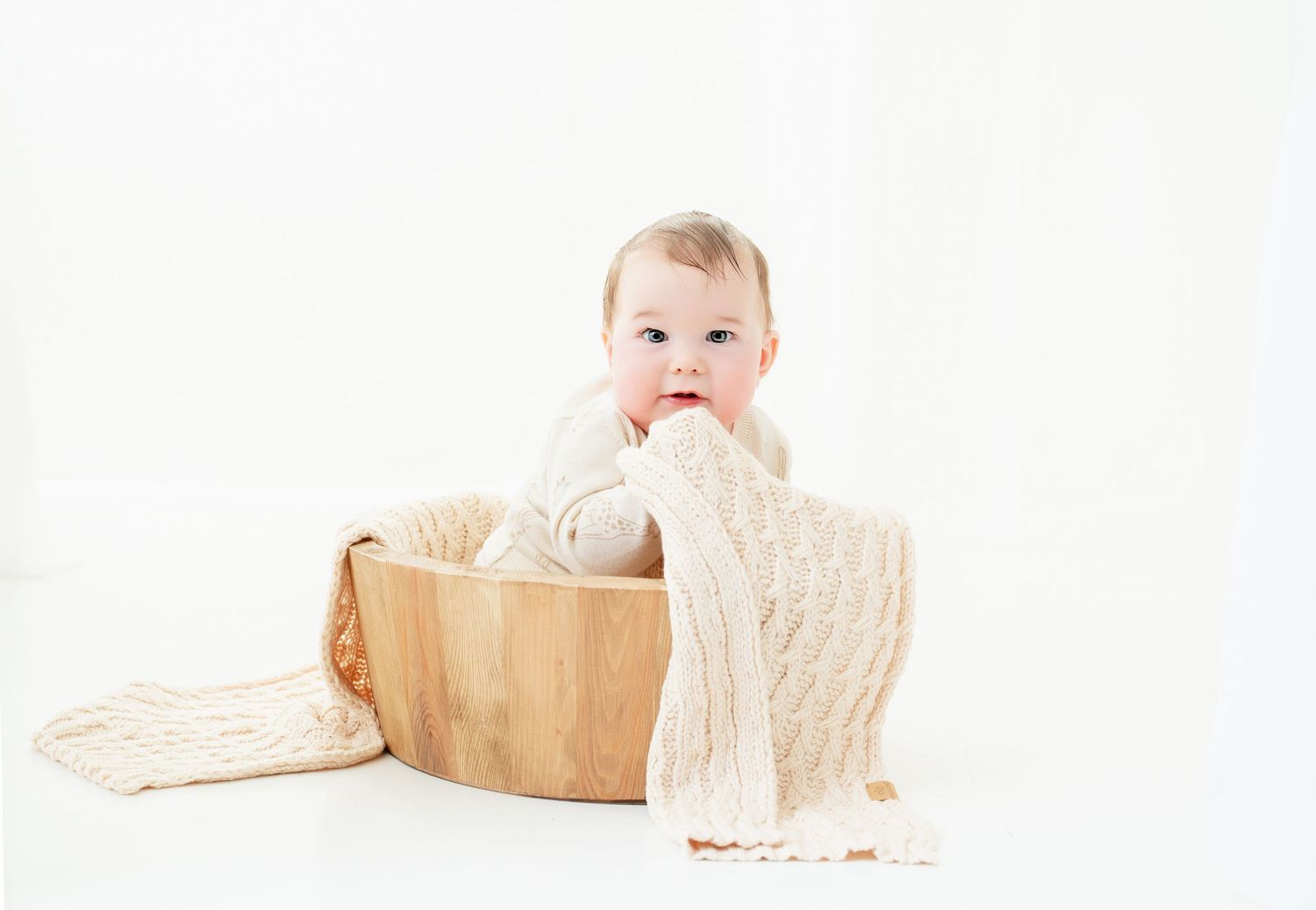 Adorable baby sitting in a wooden bowl with cream knit blanket on white background for professional portrait photography.. Minnesota milesto
