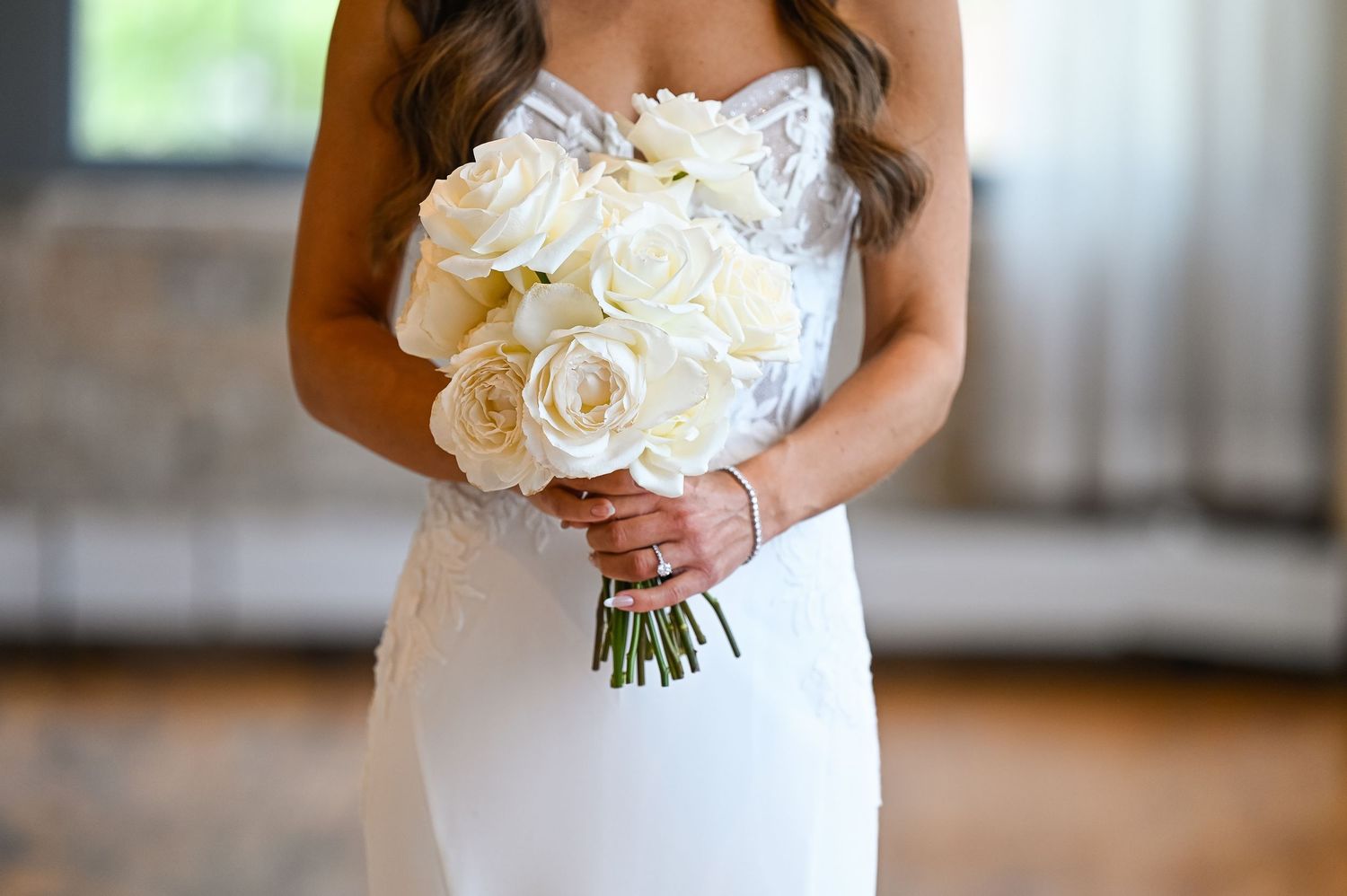 A white bridal bouquet of roses is held against an elegant white wedding dress.