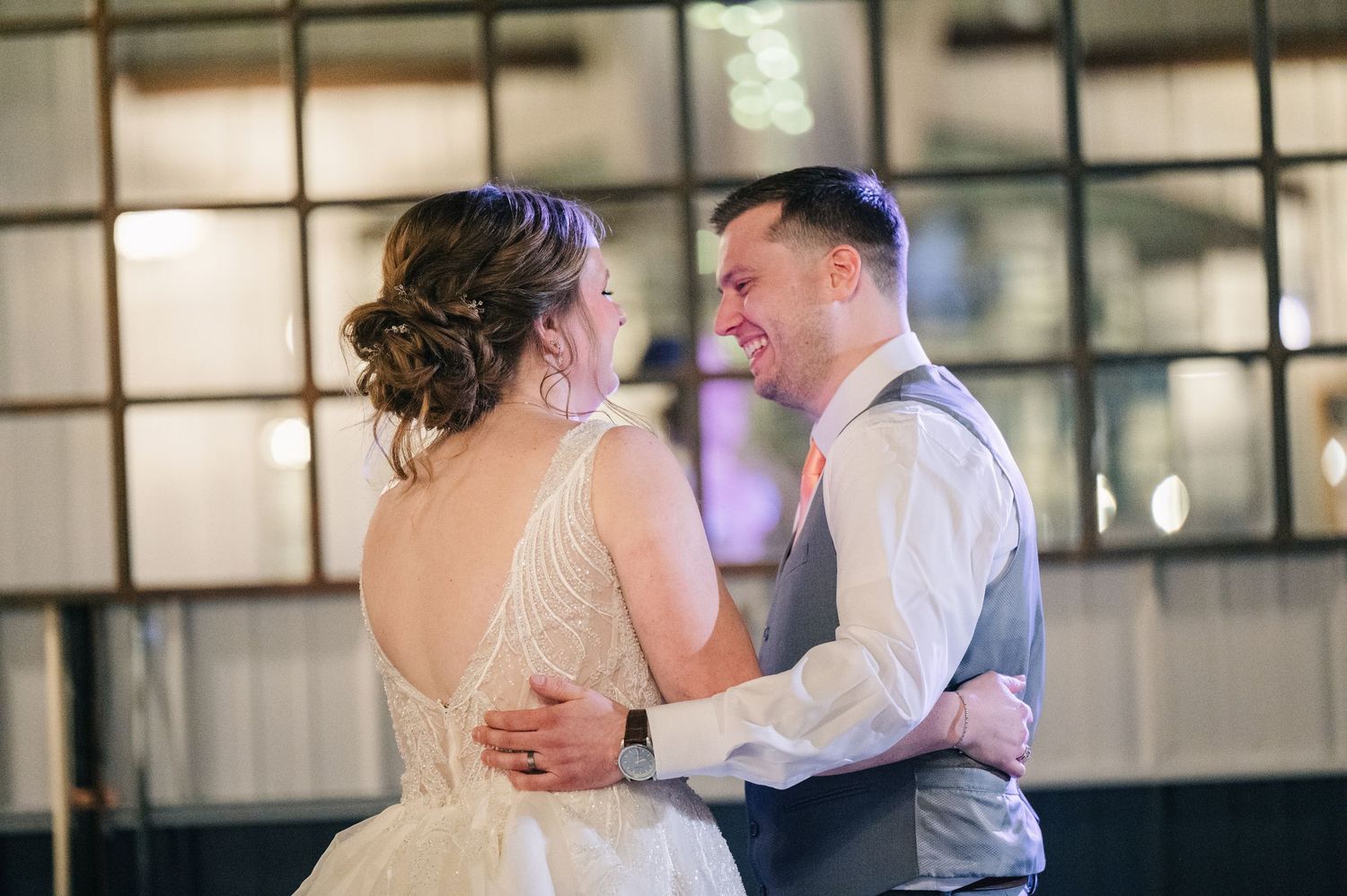 Bride and groom share intimate first dance, smiling at each other in elegant industrial wedding venue.