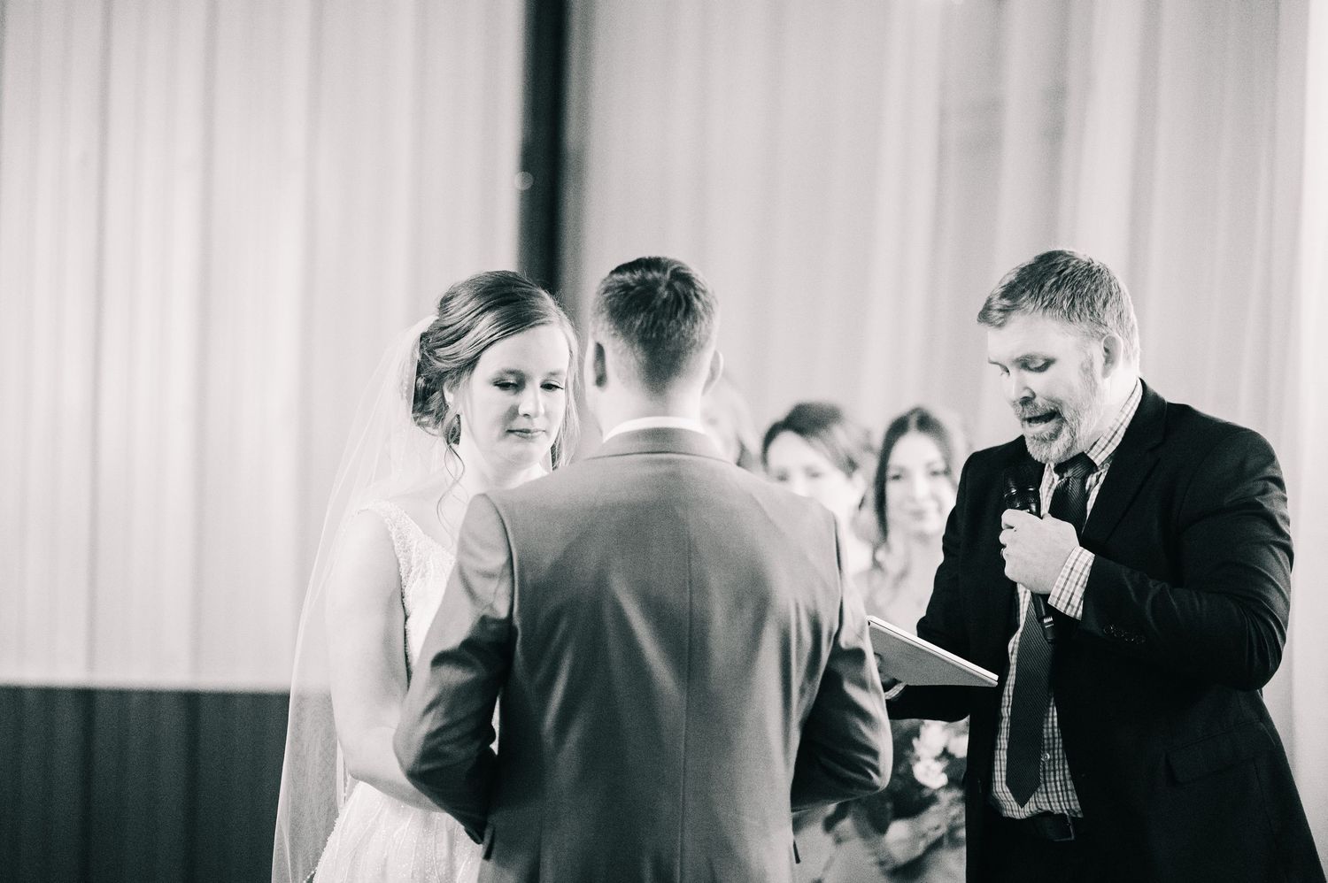 Black and white photo of officiant reading vows as bride and groom stand together during wedding ceremony.