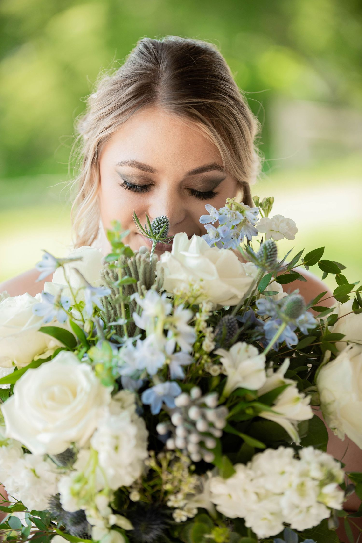 A beautiful bridal bouquet of white roses, light blue flowers and greenery captured in a close-up outdoor portrait. Zimmerman MN Weddings