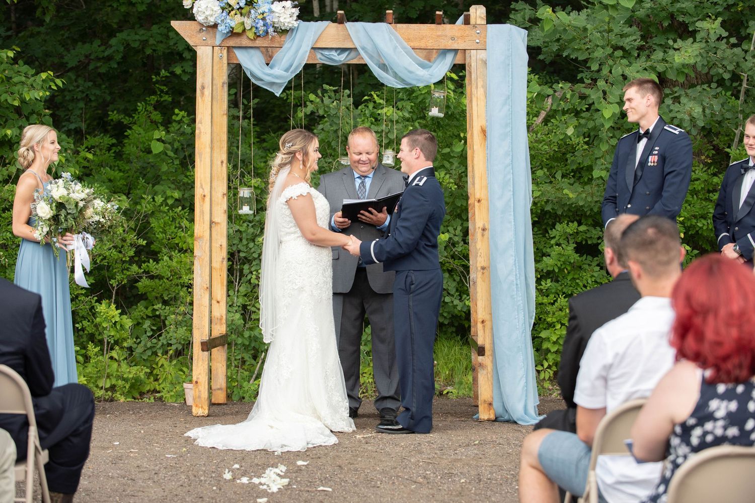 Outdoor wedding ceremony setup in a beautiful garden with wooden posts and flowing blue fabric decor. Zimmerman MN Weddings