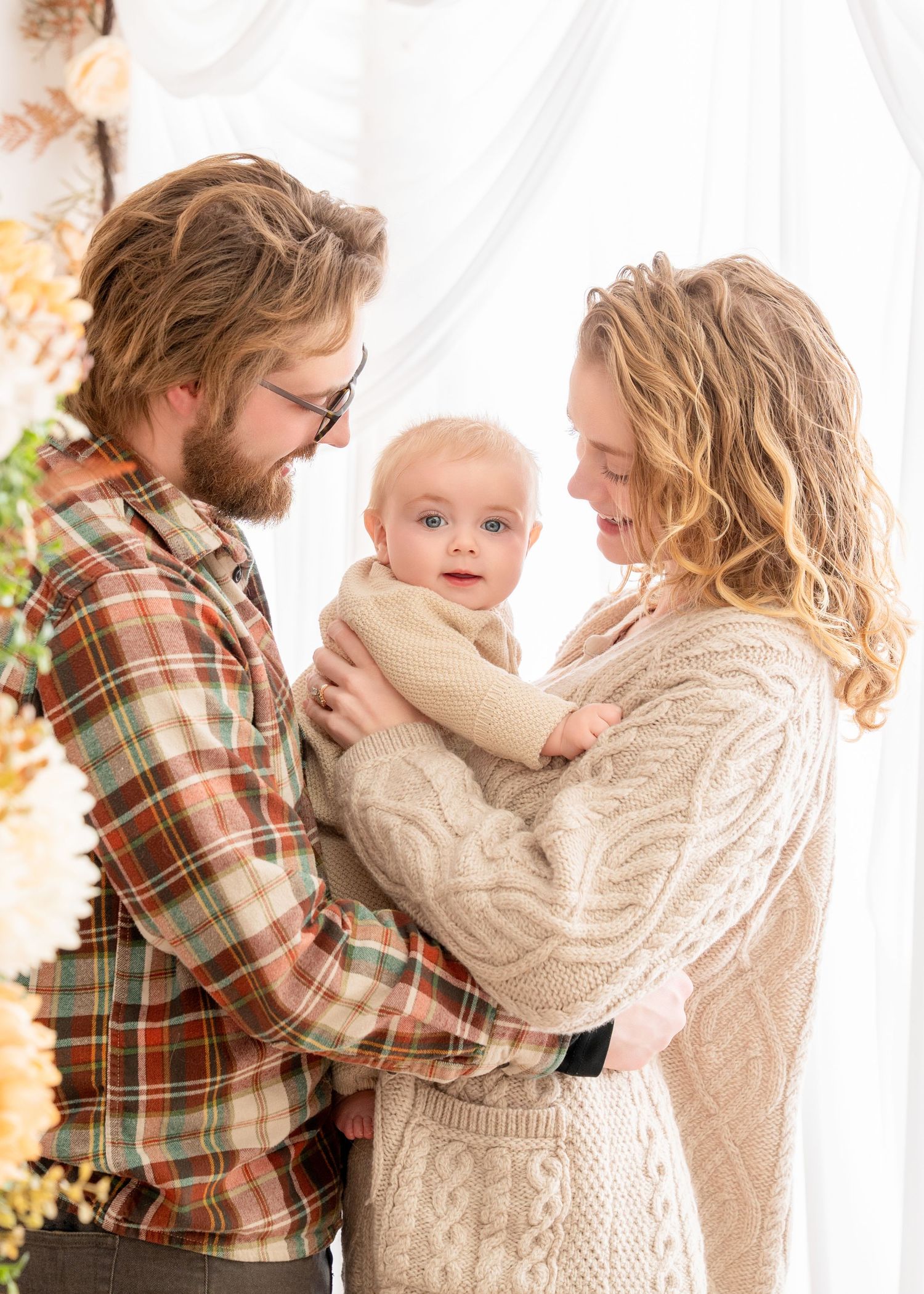 A young family shares a tender moment in front of a white backdrop while wearing cozy knit sweaters and plaid. Princeton MN Milestone, Mater