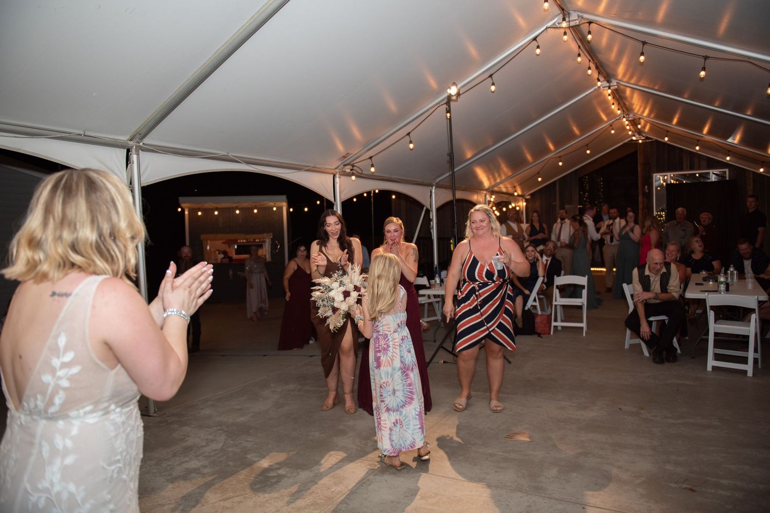 Wedding reception dance floor filled with guests under string lights in tent at night.
