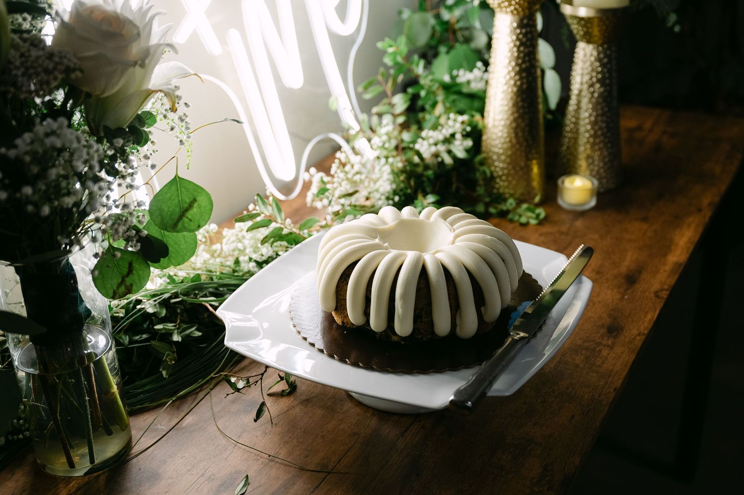 Rustic wooden table decorated with white floral arrangements and candles for an elegant event setting.