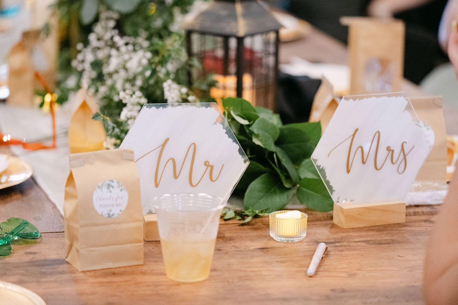 Elegant wedding place cards with calligraphy displayed on a rustic wooden table with greenery.
