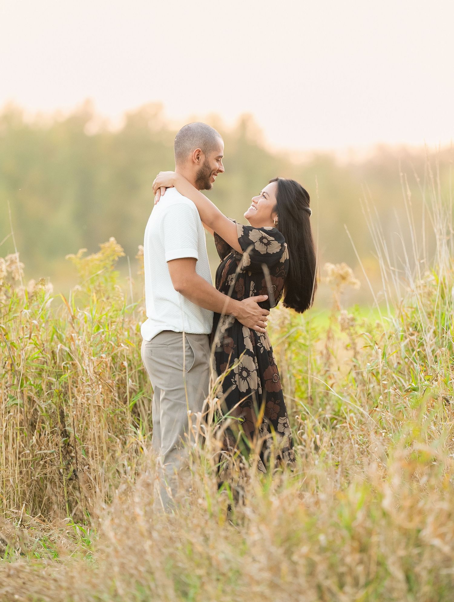 A couple shares an intimate moment in a golden field of tall grass during sunset.
