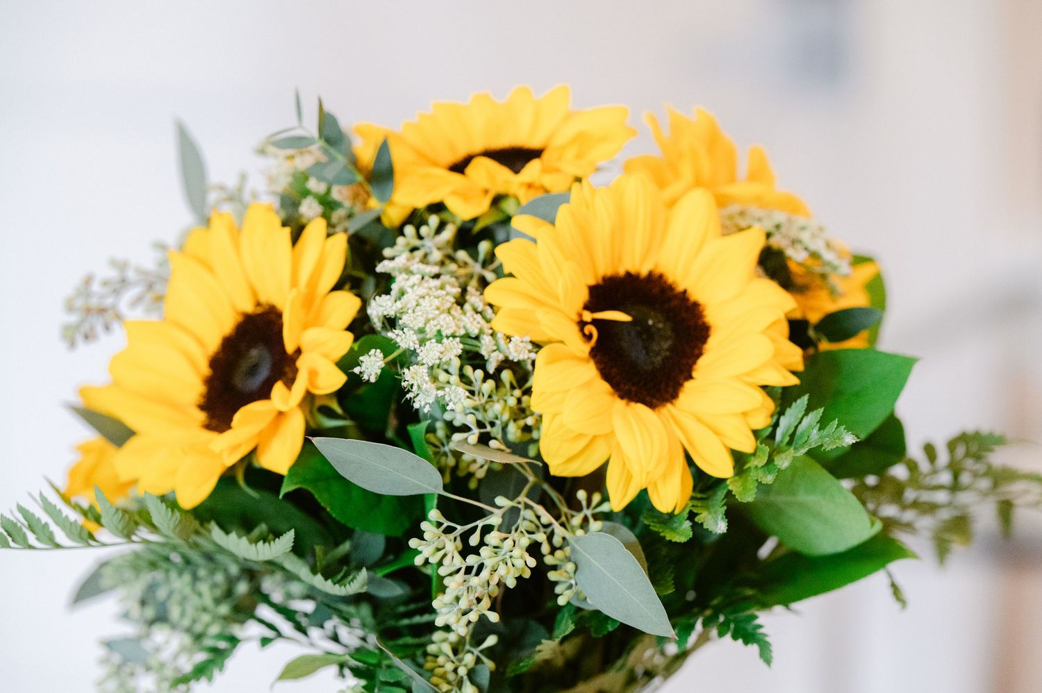Central MN Wedding Photos | Bright bridal bouquet of yellow sunflowers with white blooms and green eucalyptus leaves on a soft background.