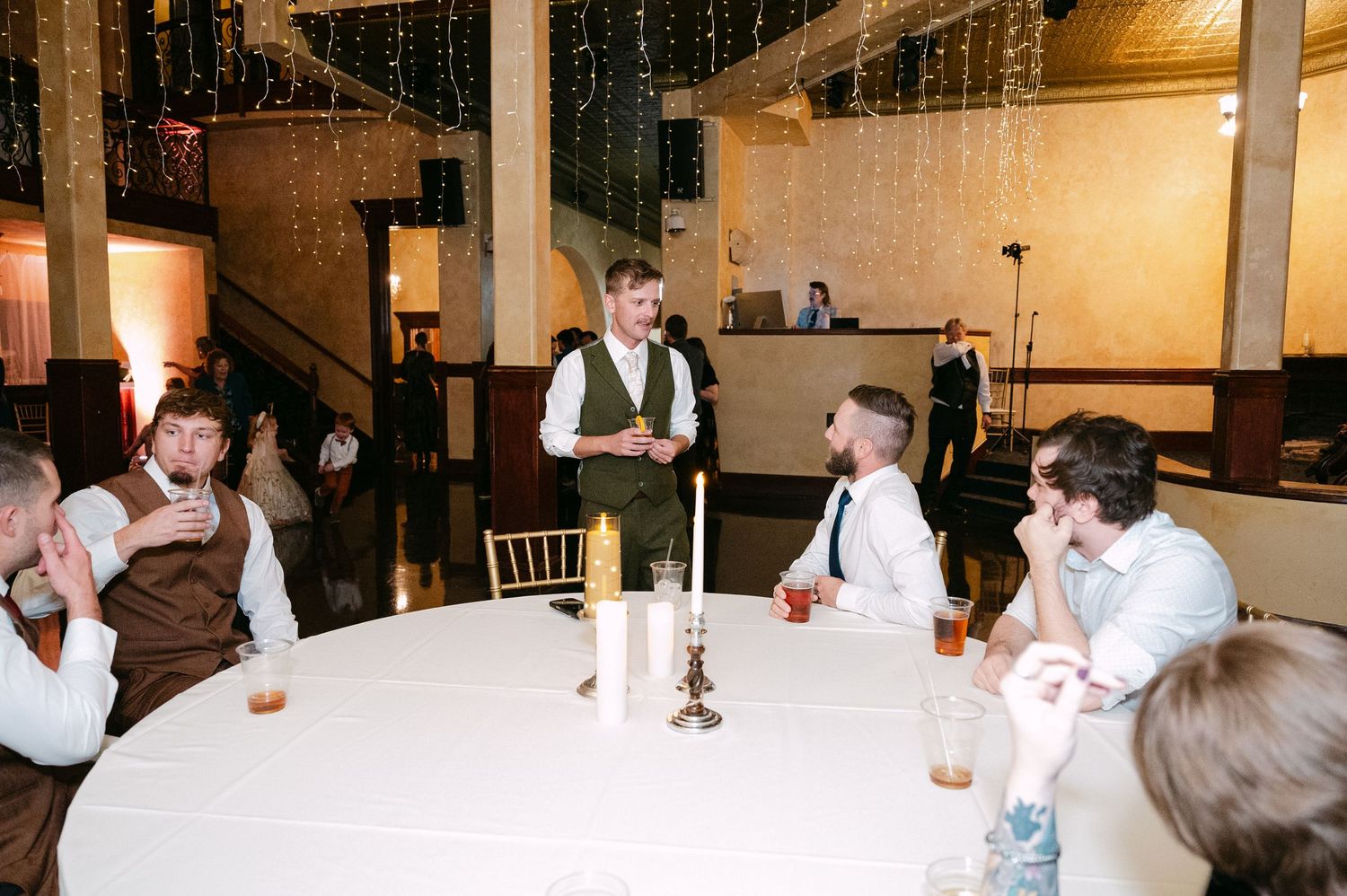 Central MN Wedding Photos | Groom toasts groomsmen at round reception table under twinkling fairy lights.