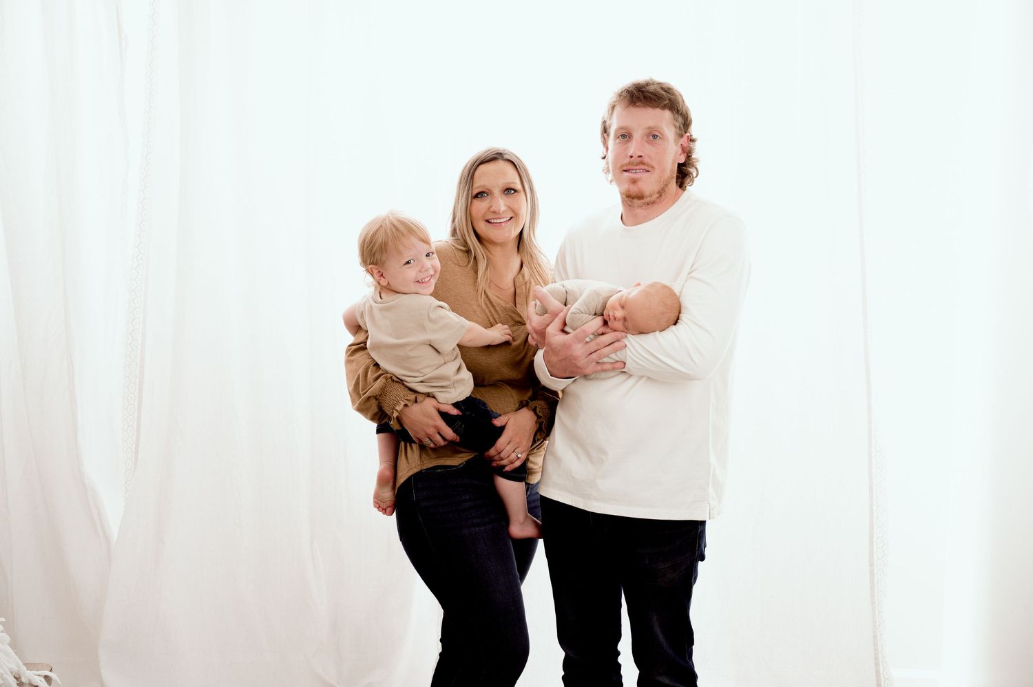 St Cloud newborn Photos of A happy family poses together, with a mother holding a toddler and father cradling a newborn in white studio.