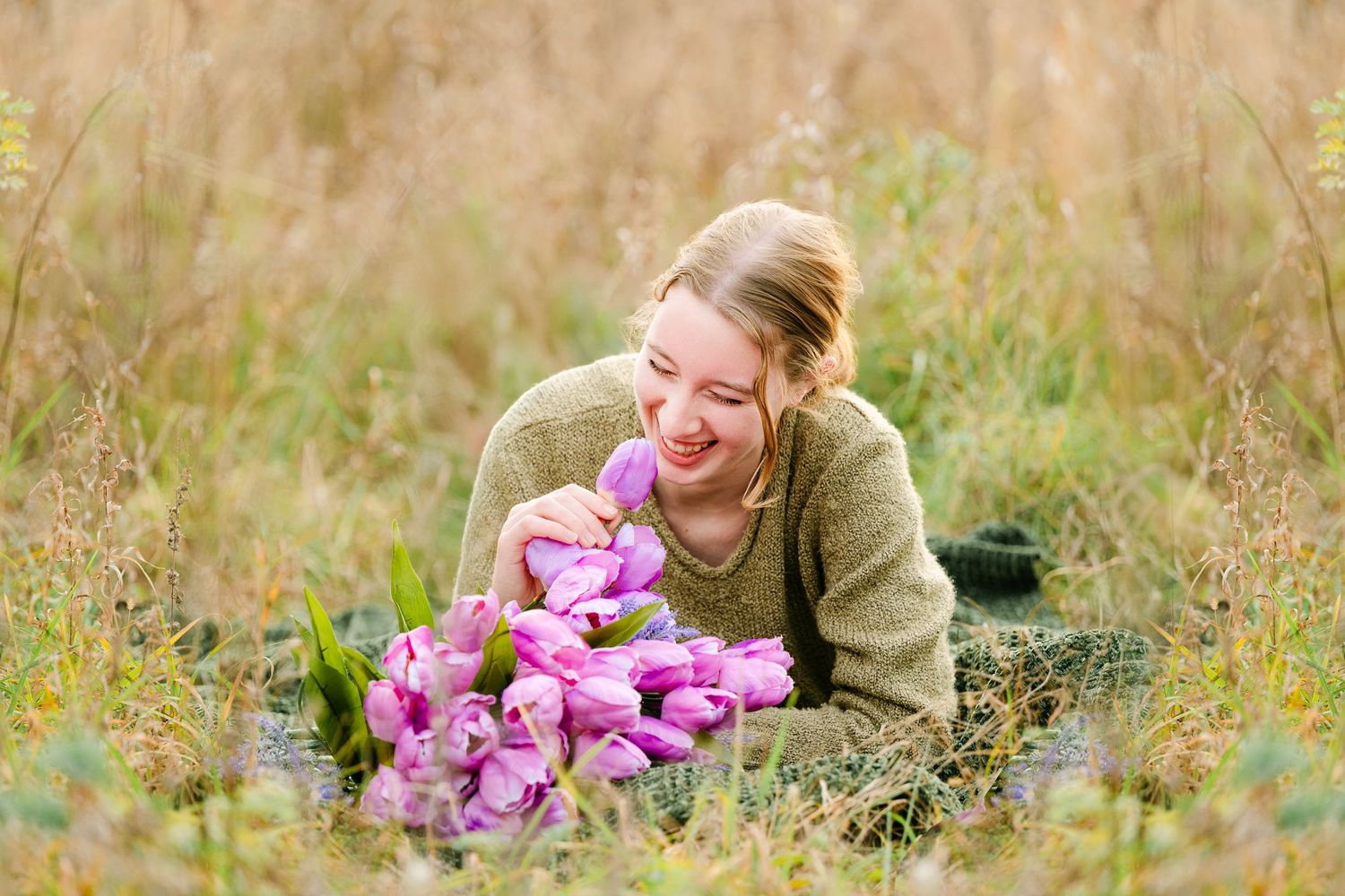 In central Minnesota a high school senior lying in golden grass field with pink flowers during a sunny autumn day.