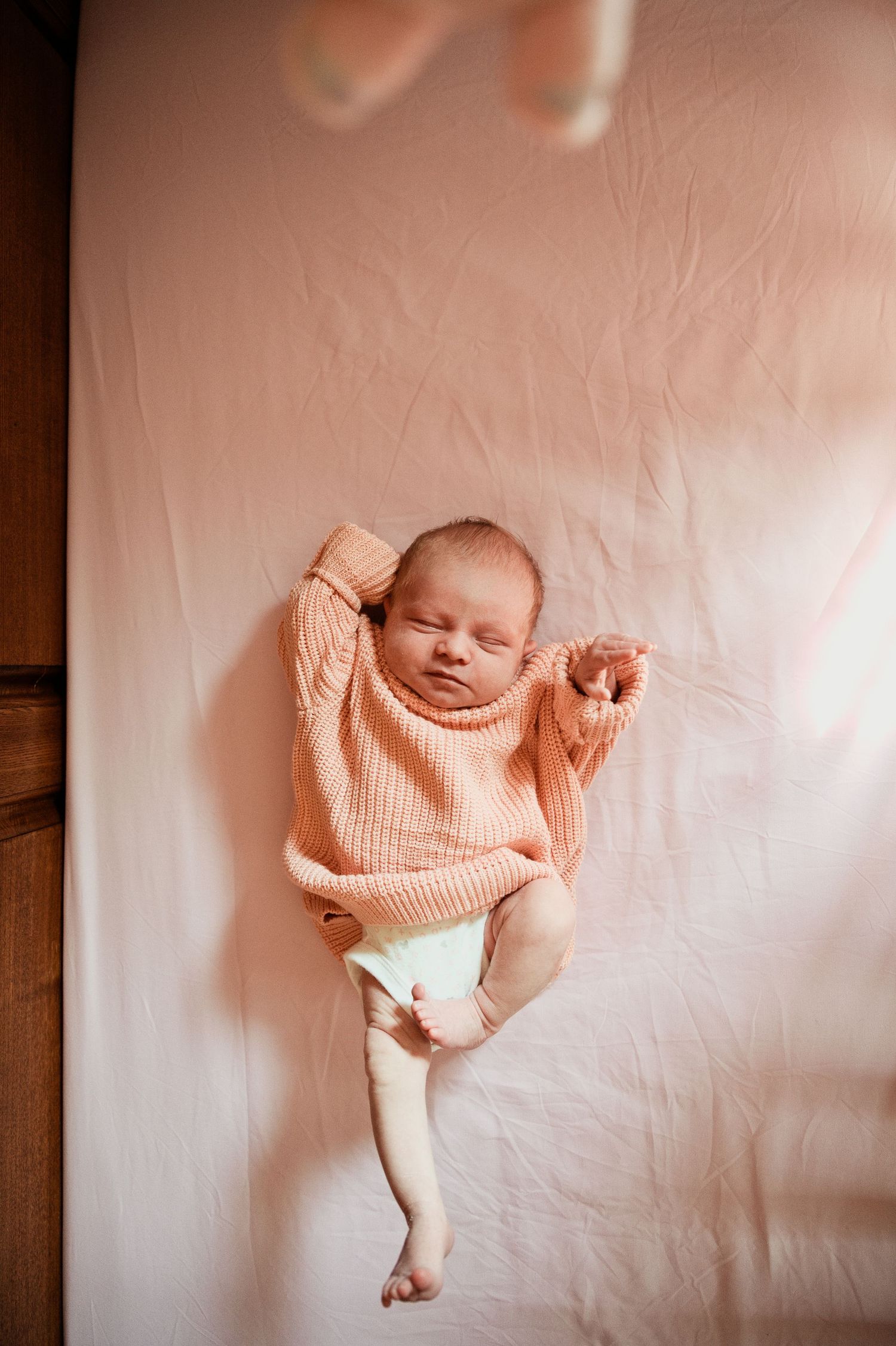 Peaceful newborn baby sleeping in a pink knit sweater and diaper on a soft blush pink blanket.