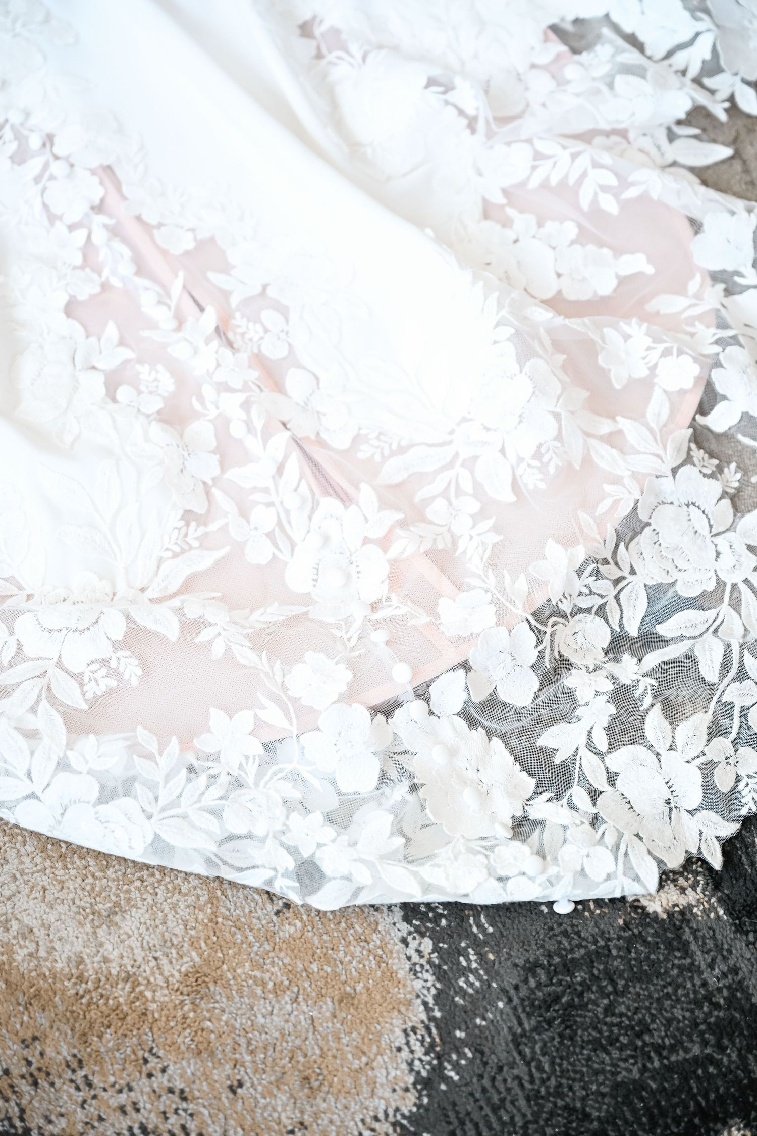 Elegant white wedding dress lace details photographed against a textured background.