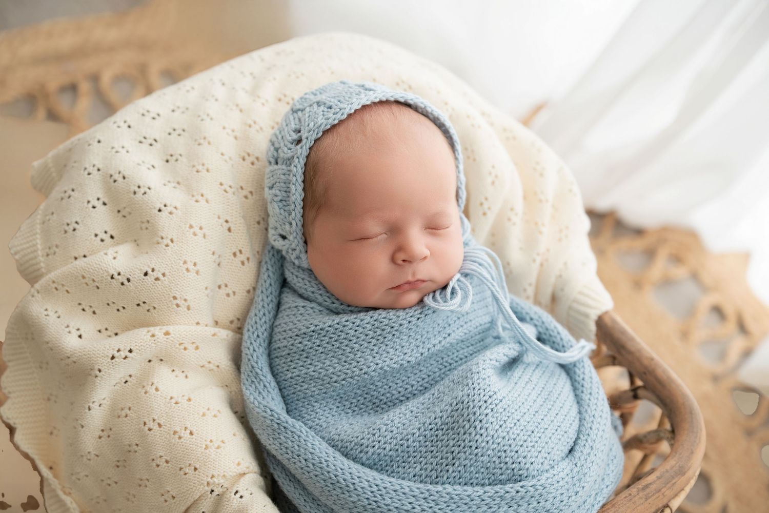 Minnesota Best newborn photographer a Sleeping newborn wrapped in soft blue knit blanket resting on cream textured cushion in natural light.