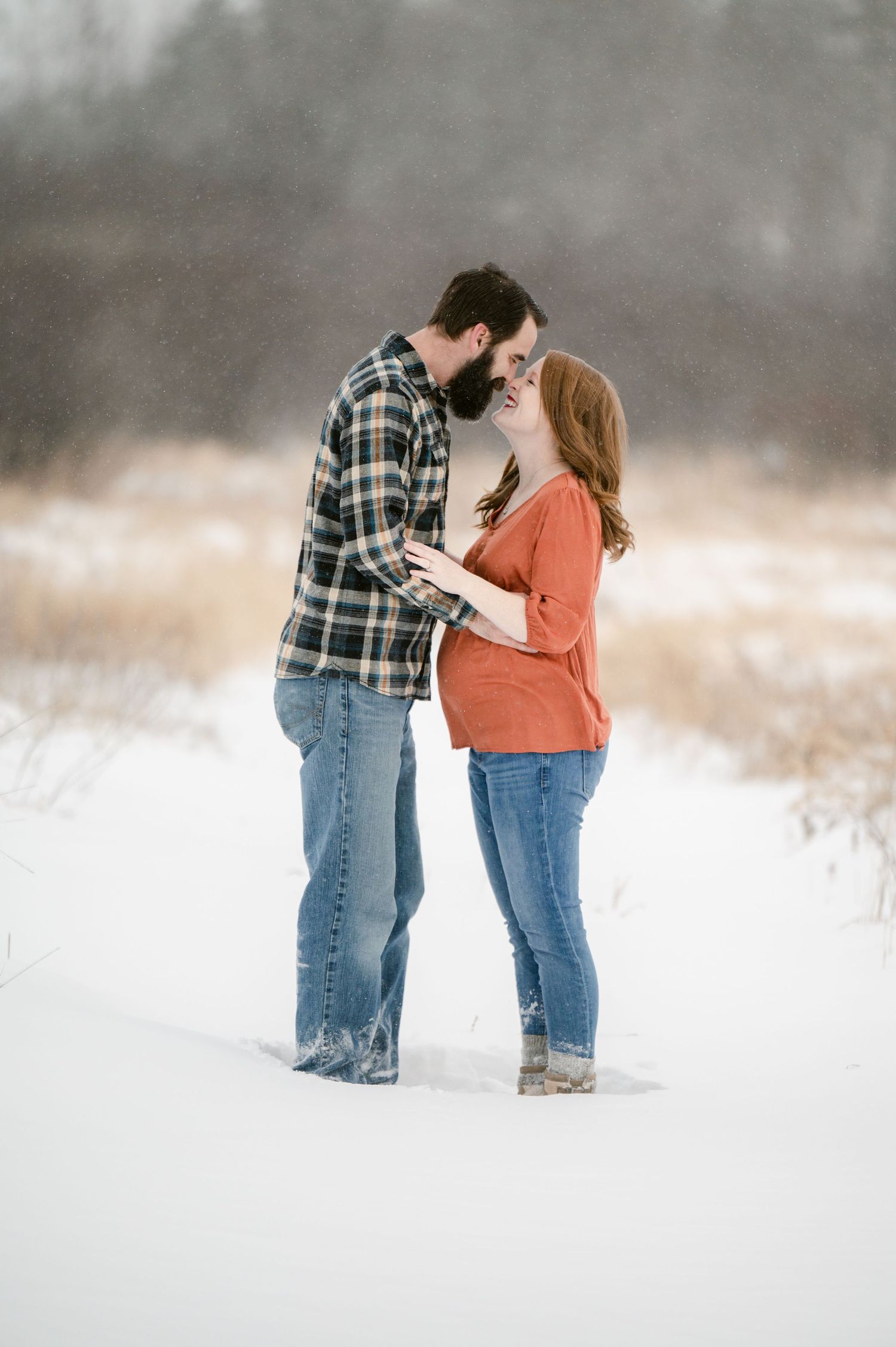 The Clark’s romantic winter maternity photoshoot series. A couple in casual winter attire sharing tender moments in a snow-covered field.
