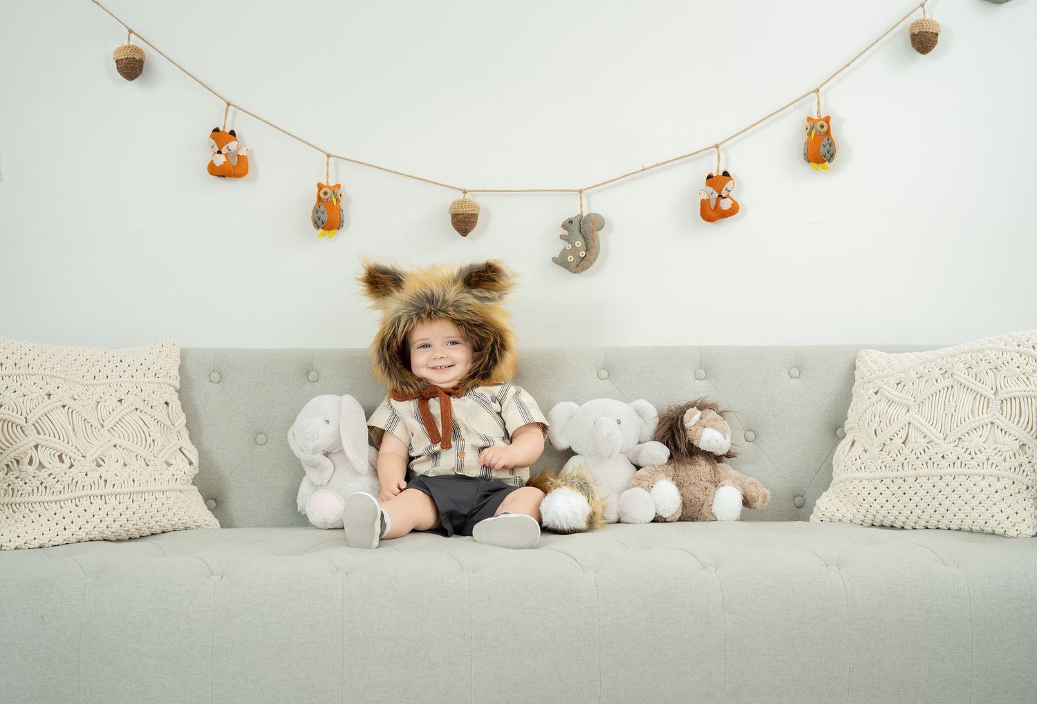 A cozy gray couch with plush toys and decorative woodland themed bunting banner hanging above. Princeton MN Milestone, Maternity and Newborn