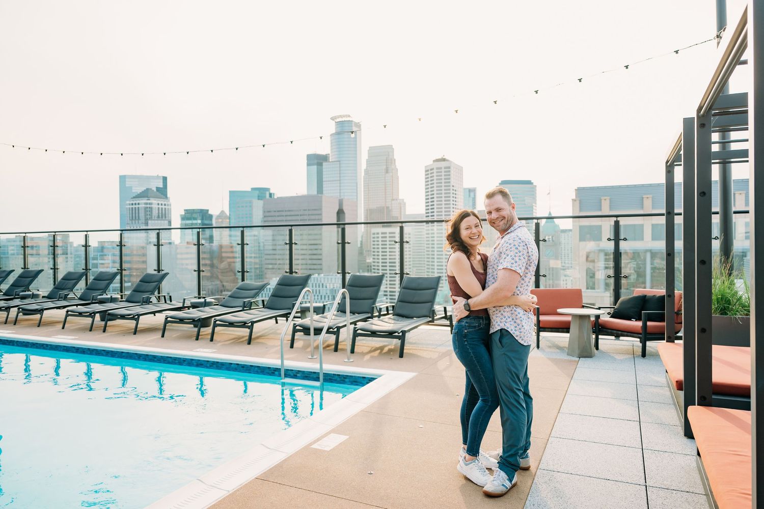 A rooftop terrace with lounge chairs and city skyline views features string lights overhead.