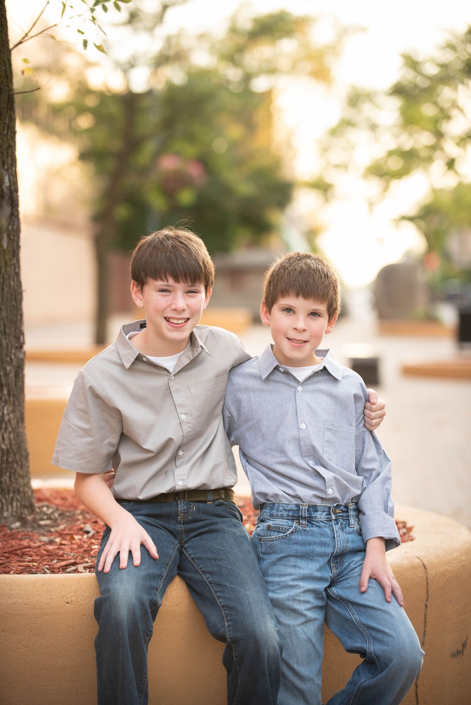 Children in button-down shirts and jeans share a laugh while sitting together on a concrete ledge.