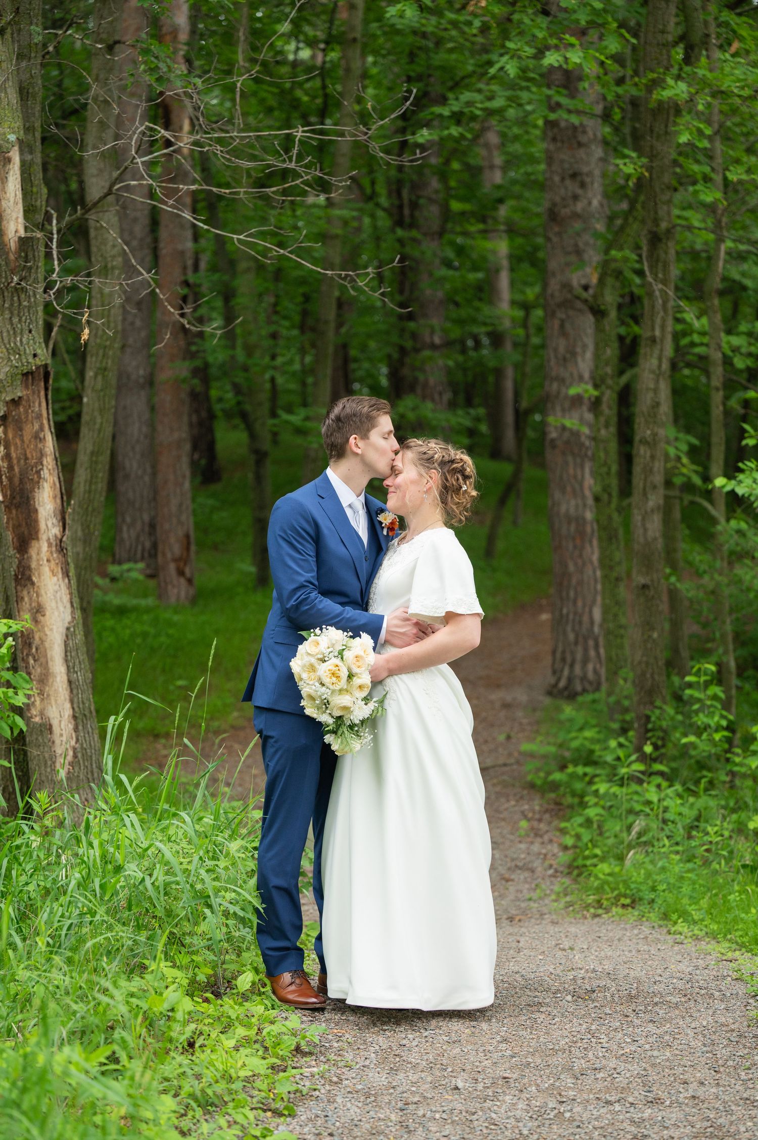 Romantic wedding portraits on a tree-lined path in a forest setting.