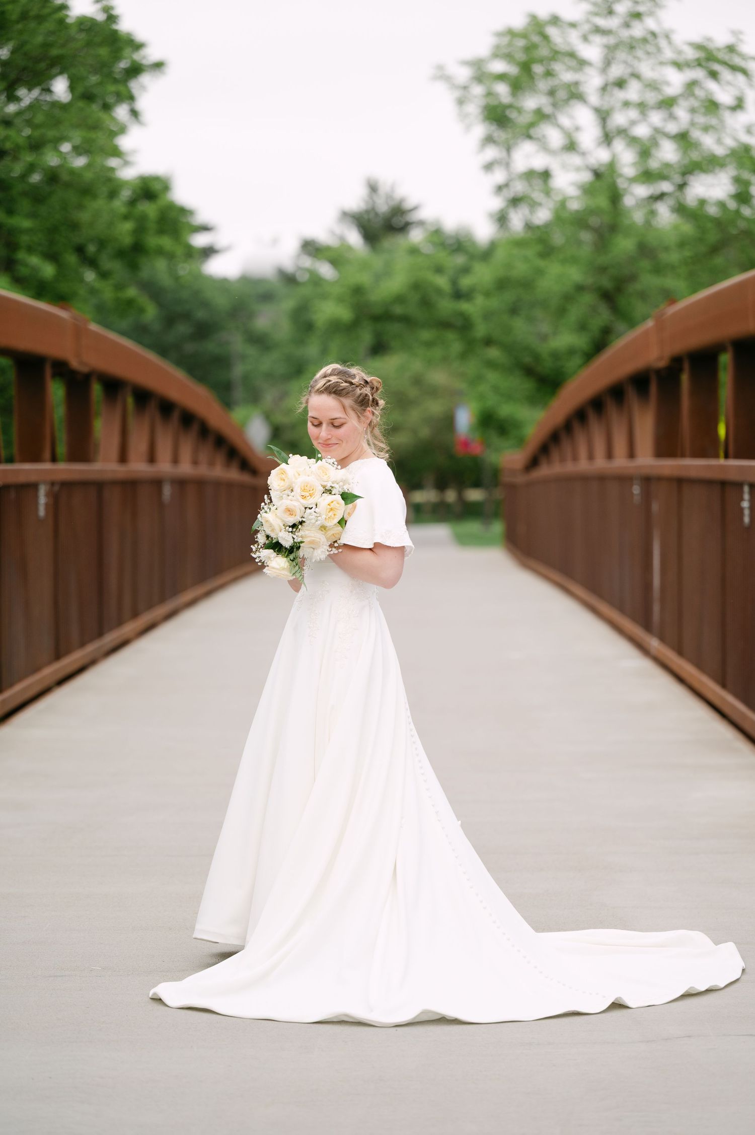 A flowing white wedding dress photographed on a rustic wooden bridge surrounded by lush greenery.