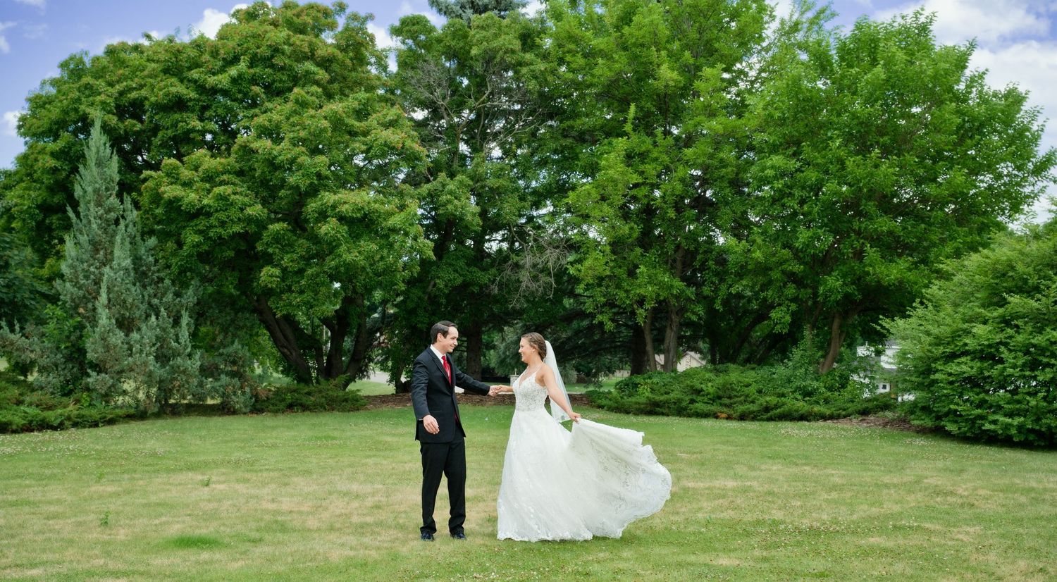 Bride and groom share a joyful moment as her wedding dress flows in a lush green garden.