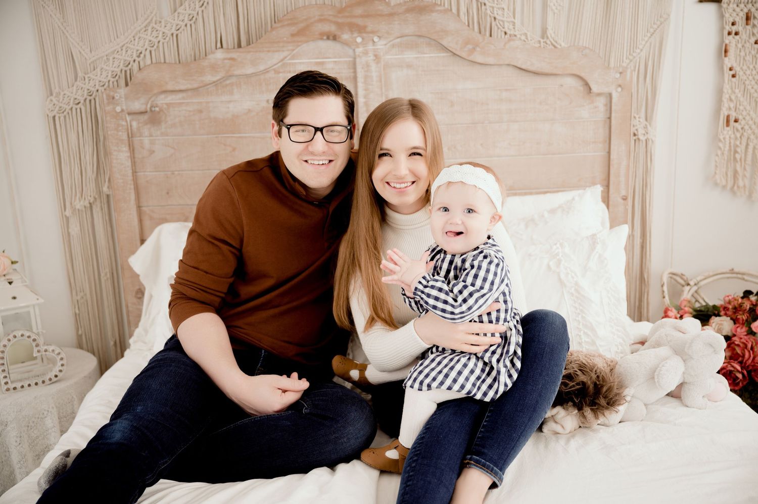 Family portrait on bed with rustic wooden headboard in warm neutral tones.