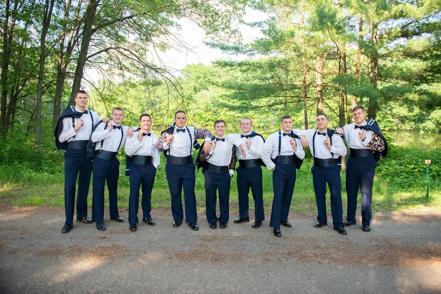 Groomsmen in navy uniforms standing in line on a forest path. Zimmerman MN Weddings