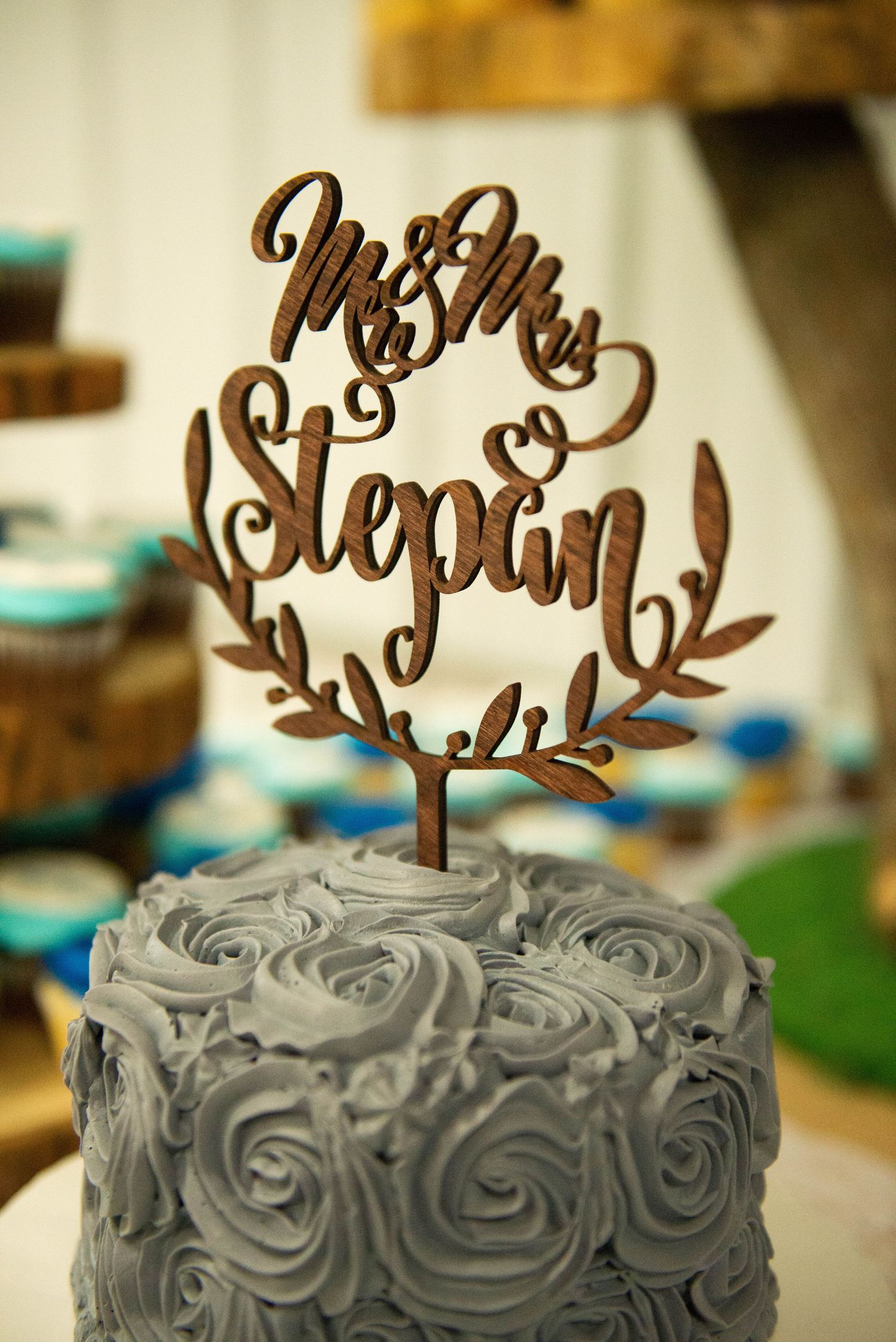 Three gray frosted wedding cakes feature elegant brown wooden cake toppers with cursive text decorations. Zimmerman MN Weddings