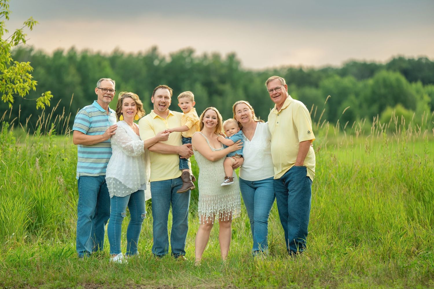 A loving multigenerational group poses together in a sunny green meadow on a summer evening.